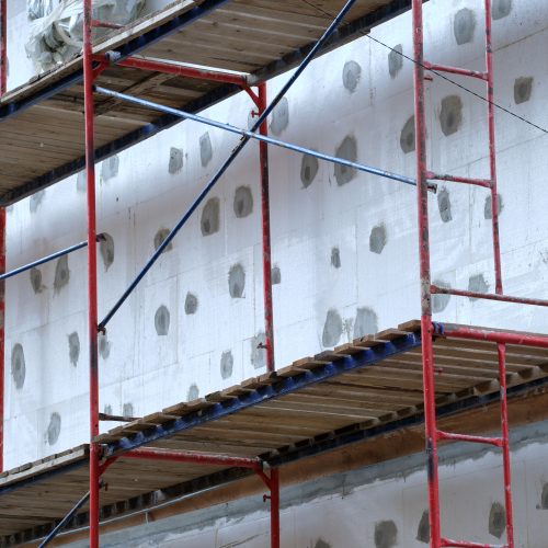 Building facade under renovation works with construction scaffolding frame. Wall insulation with styrofoam sheets for energy efficient home