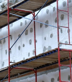 Building facade under renovation works with construction scaffolding frame. Wall insulation with styrofoam sheets for energy efficient home