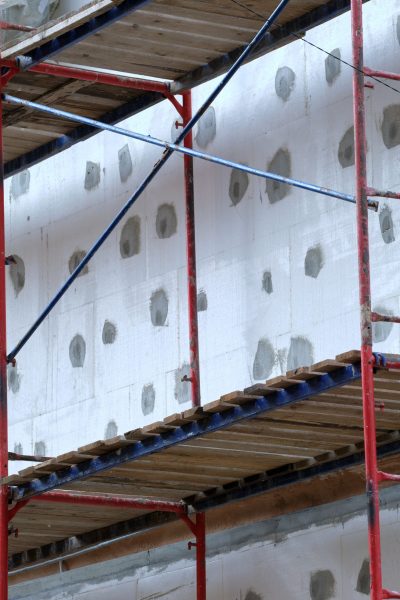 Building facade under renovation works with construction scaffolding frame. Wall insulation with styrofoam sheets for energy efficient home